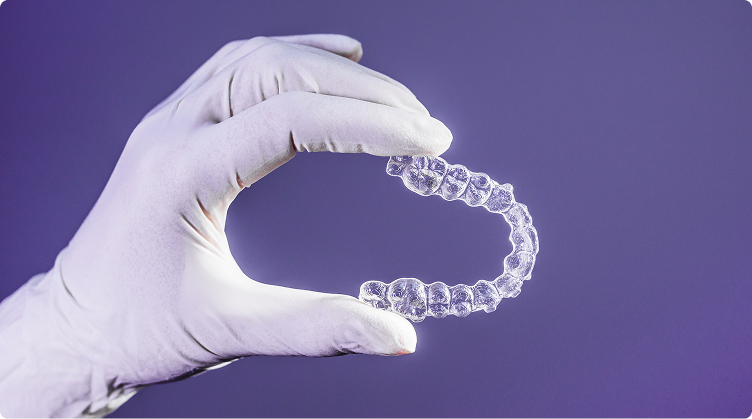 Dental professional wearing white gloves holding a clear Invisalign aligner